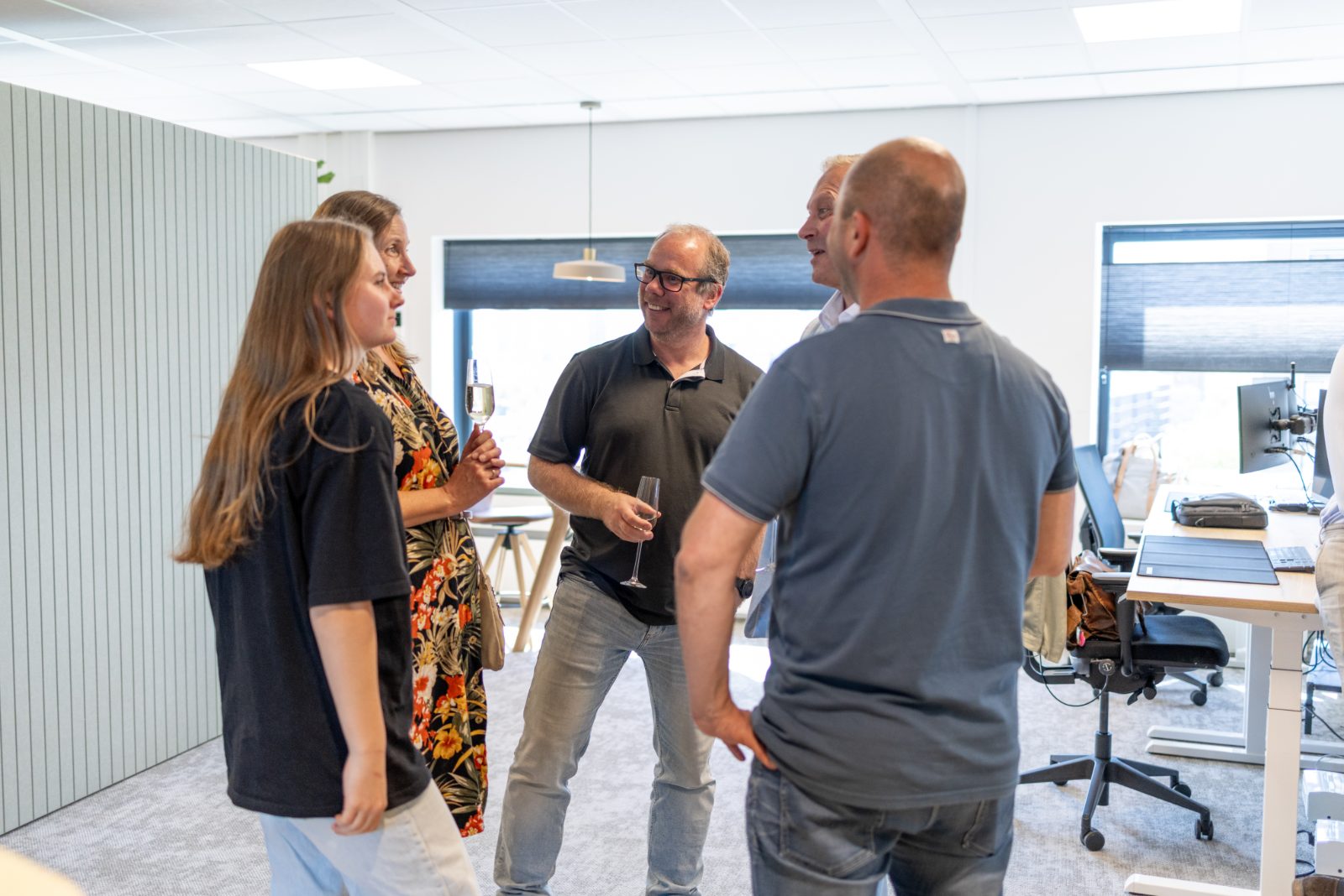Vijf collega's staan in een kring te praten tijdens een borrel op kantoor.