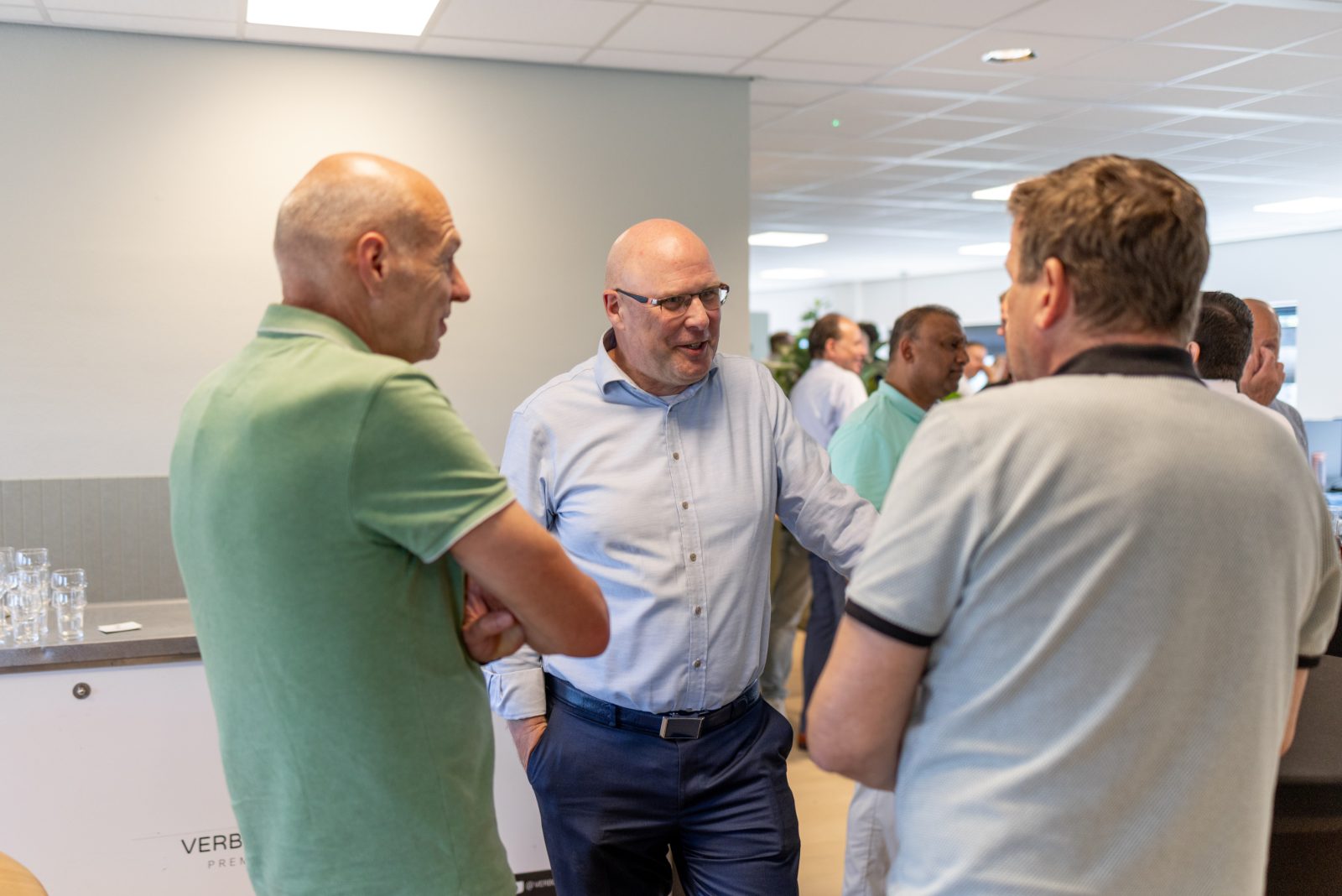 Drie mannen in gesprek bij de pantry tijdens een borrel op kantoor.