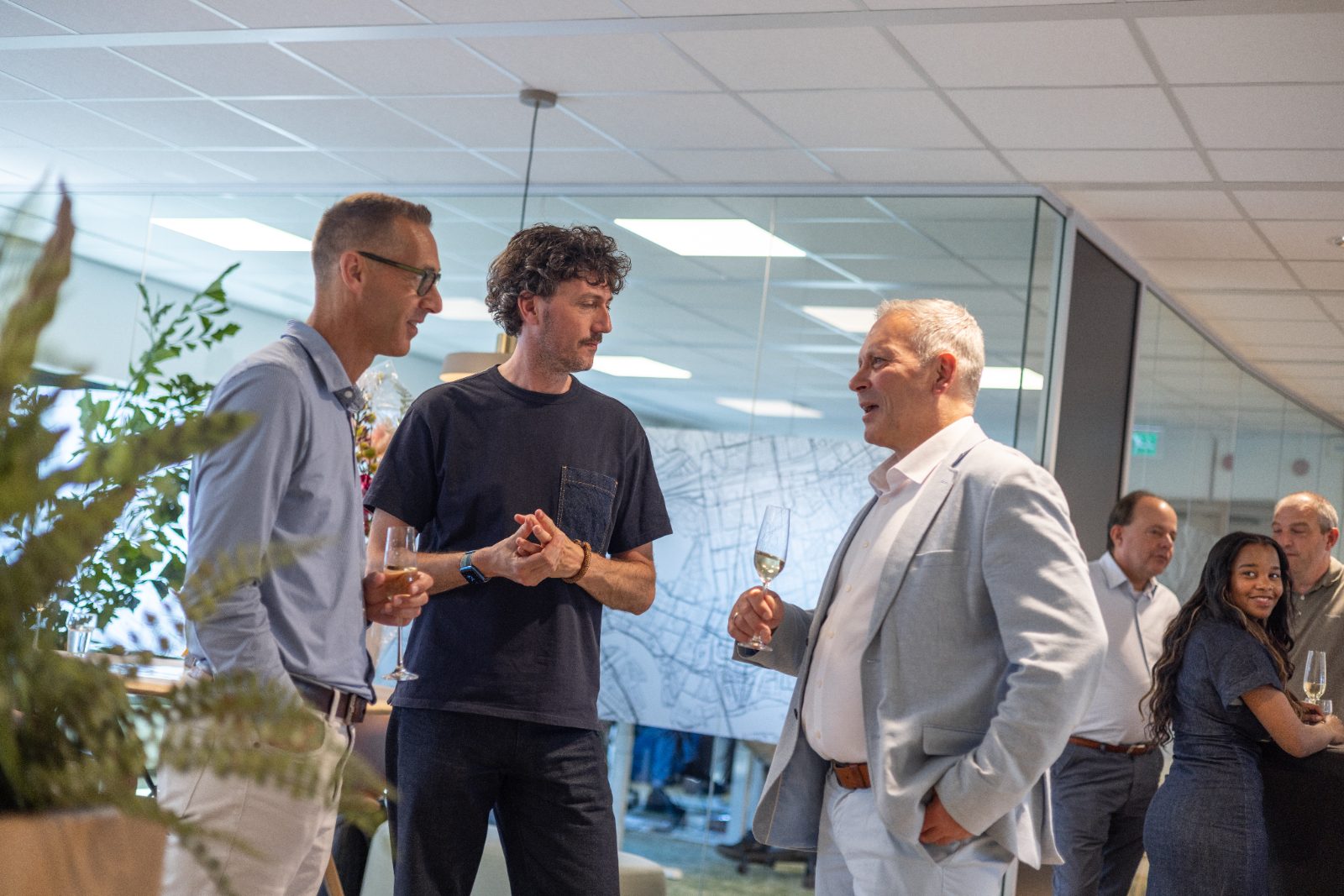 Drie mannen in geanimeerd gesprek met een glas bubbels op kantoor.