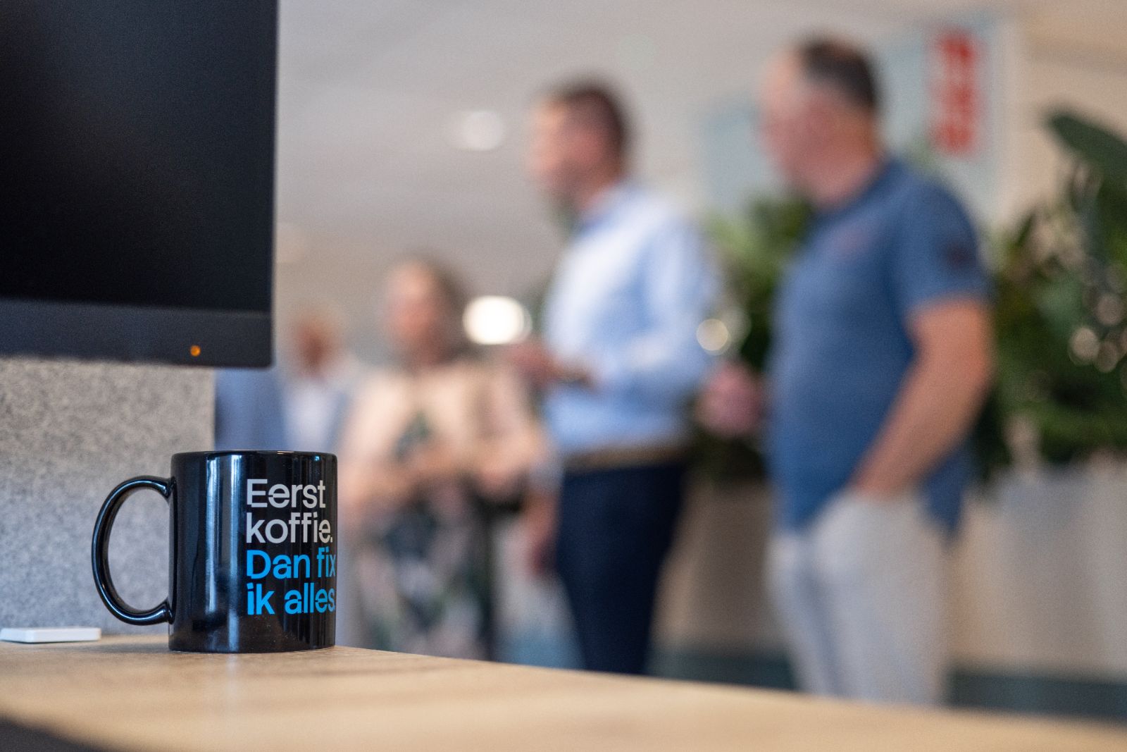 Zwarte koffiemok met tekst Eerst koffie, dan fix ik alles op een kantoorbalie.