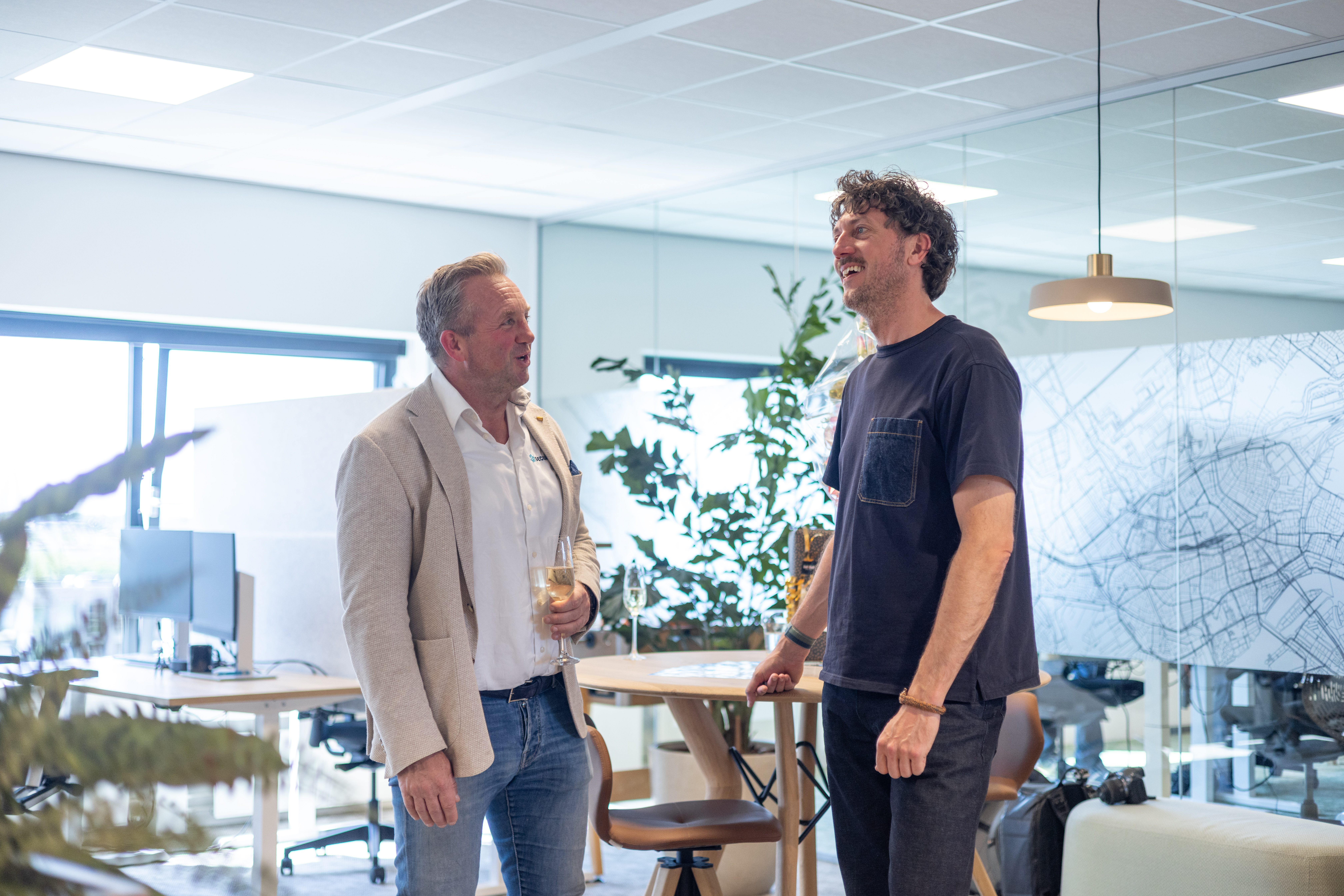 Twee mannen in gesprek tussen de bureaus, bij een wand met een plattegrond van Rotterdam.