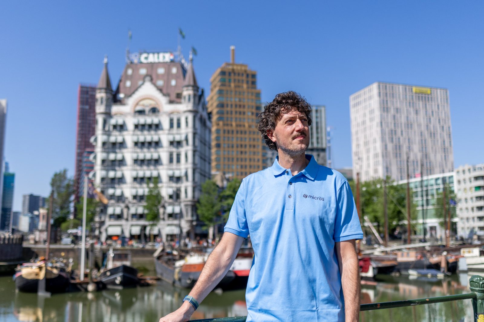 Man in Micros-polo leunt aan de Oude Haven en kijkt weg, Het Witte Huis onscherp achter hem.