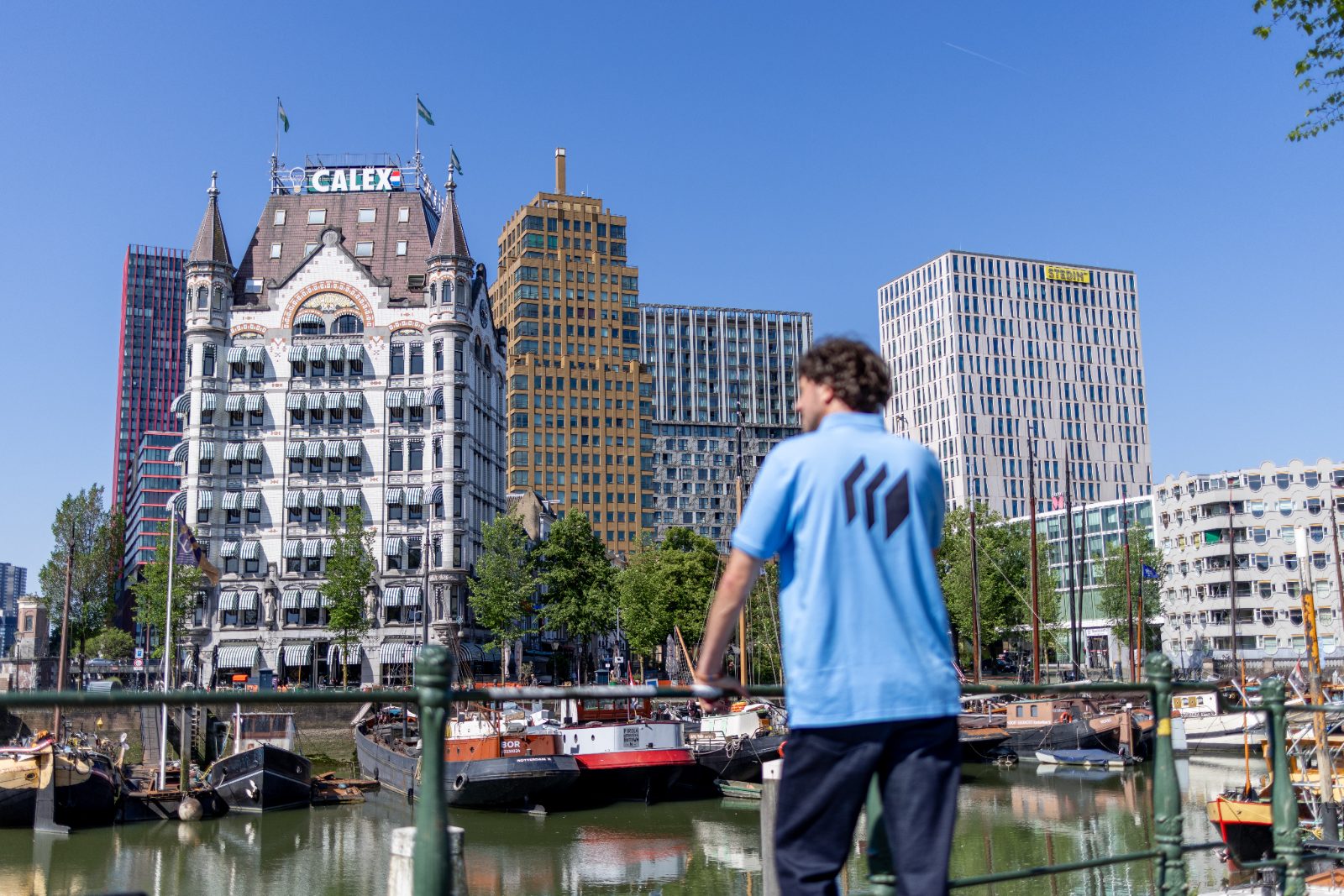 Man in blauwe Micros-polo kijkt over de Oude Haven naar Het Witte Huis in Rotterdam.