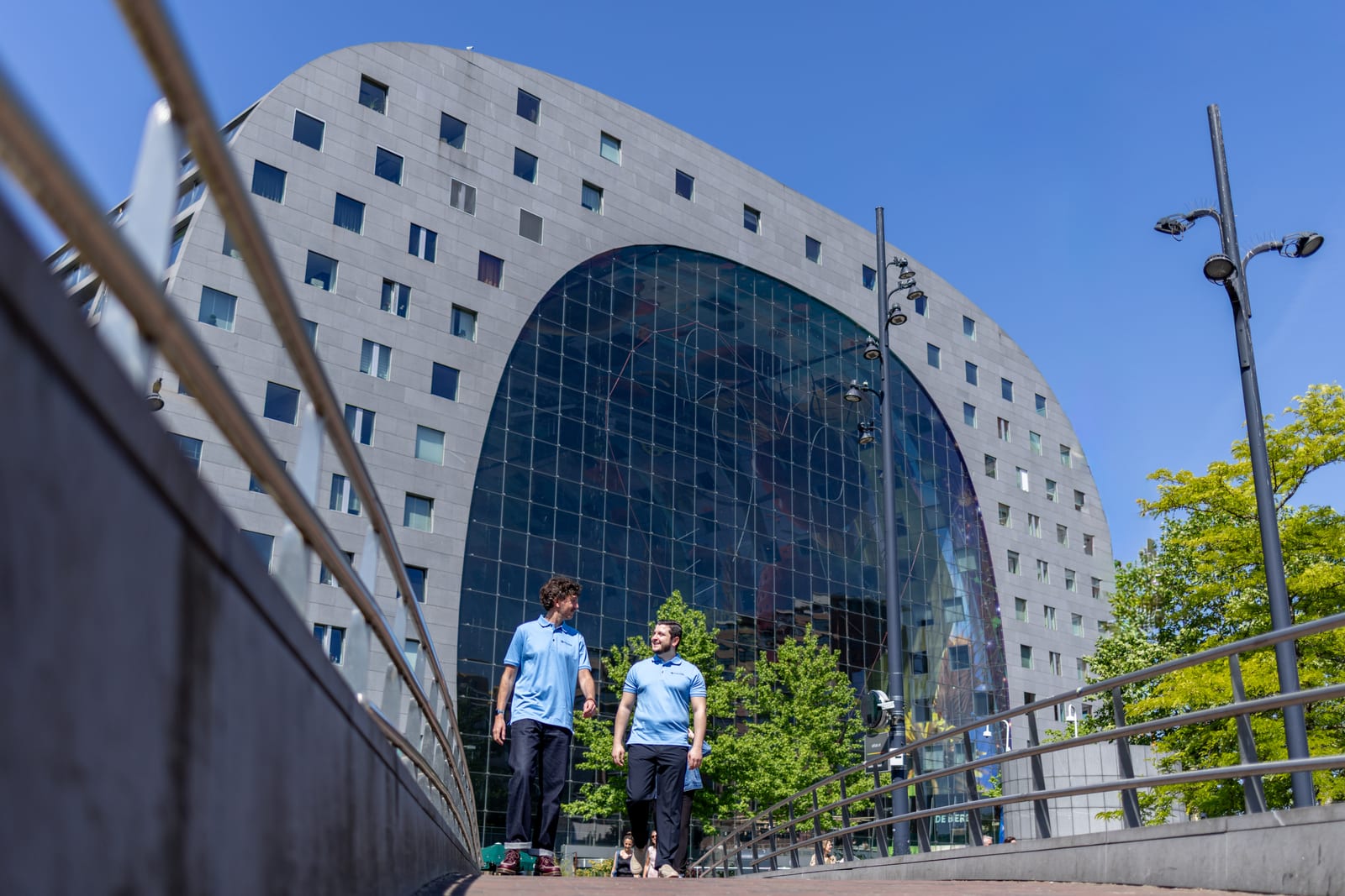Twee Micros-medewerkers lopen pratend voor de Markthal in Rotterdam.