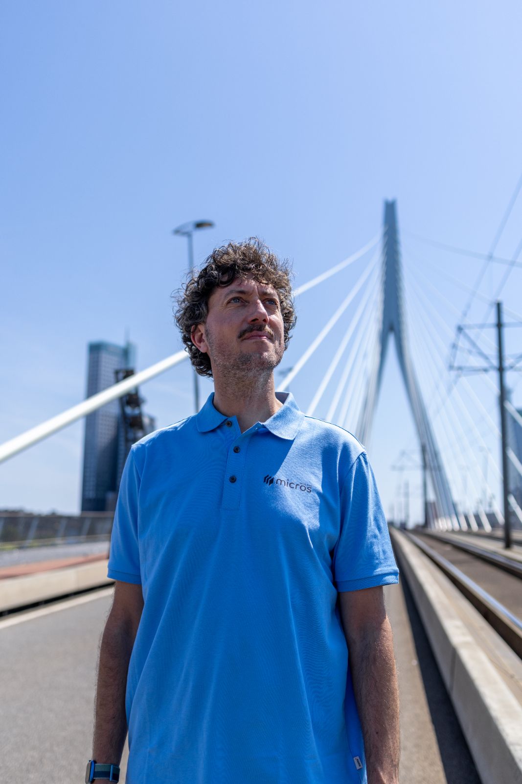 Micros-medewerker in lichtblauwe polo op de Erasmusbrug in Rotterdam.
